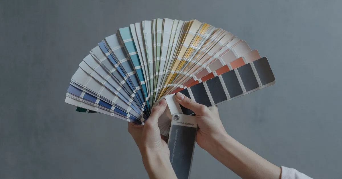 Hands holding a colorful fan of swatches on a gray backdrop, ideal for design themes.
