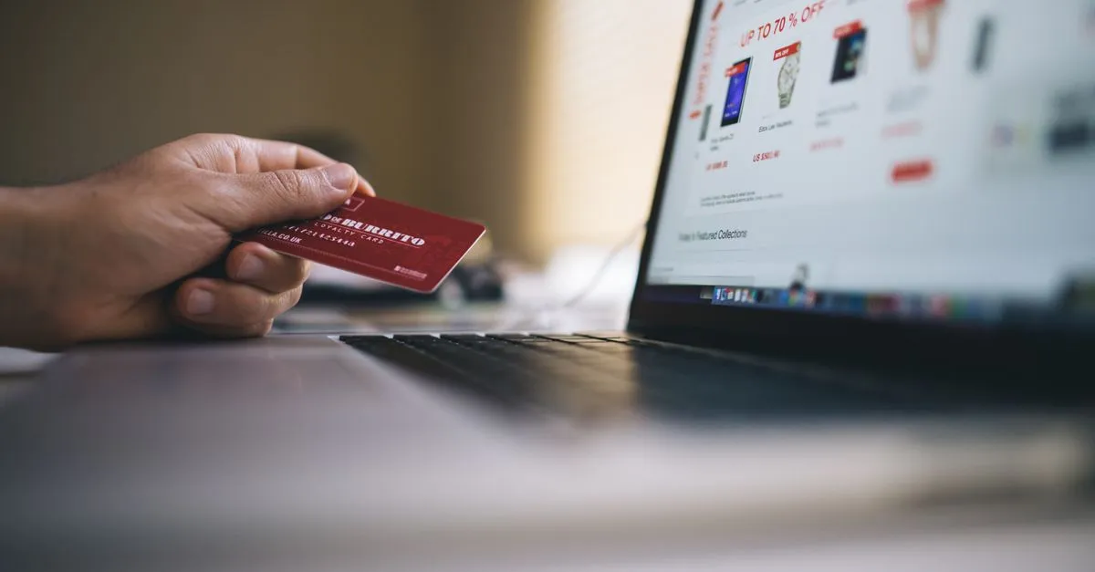 Person holding a credit card while shopping online on a laptop, indicating ecommerce transactions.