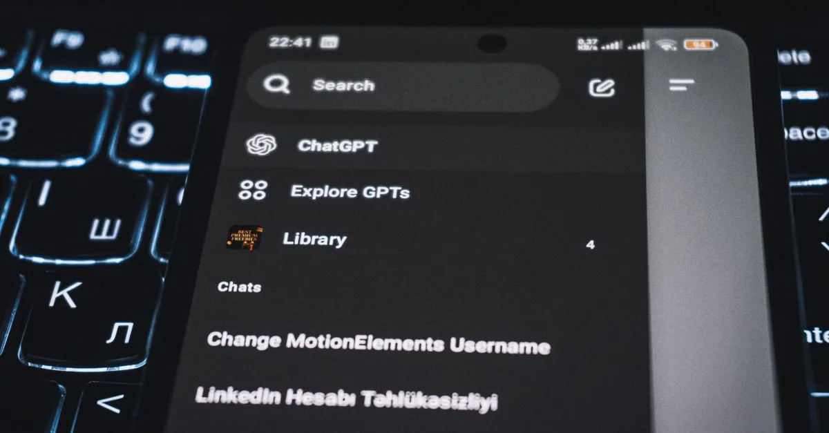 Close-up of a smartphone displaying a chat app interface with a backlit keyboard in the background.