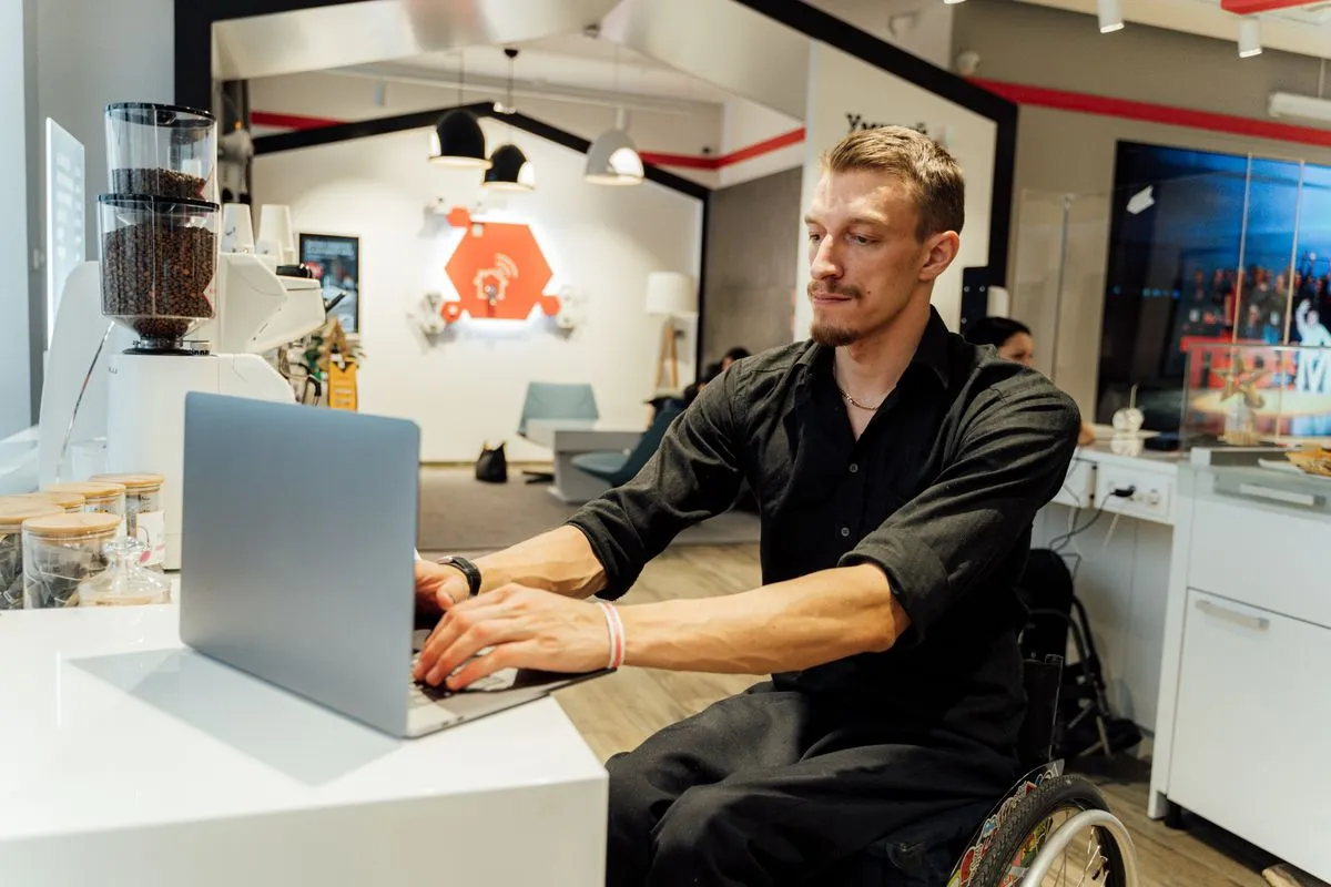 Man in a wheelchair using a laptop in a modern cafe, showcasing accessibility.