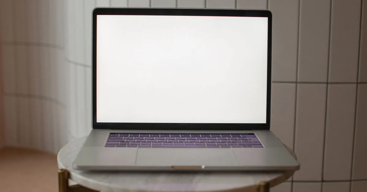 A laptop with a blank screen is positioned on a small round table, ideal for mockup use.