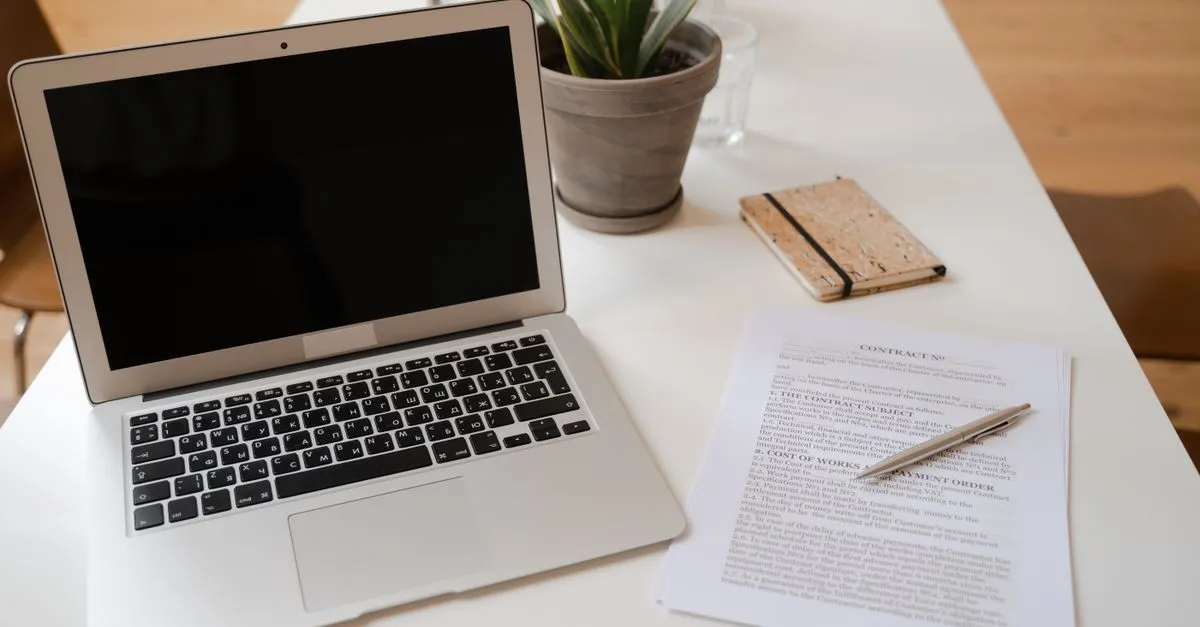 A serene office desk setup featuring a laptop, plant, and contract document ideal for business themes.