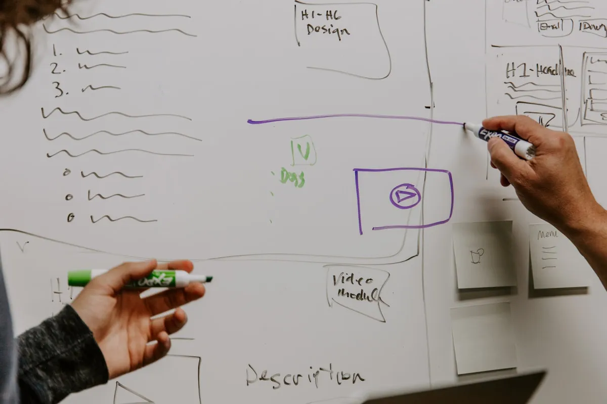 Two designers collaborating at a whiteboard during website planning
