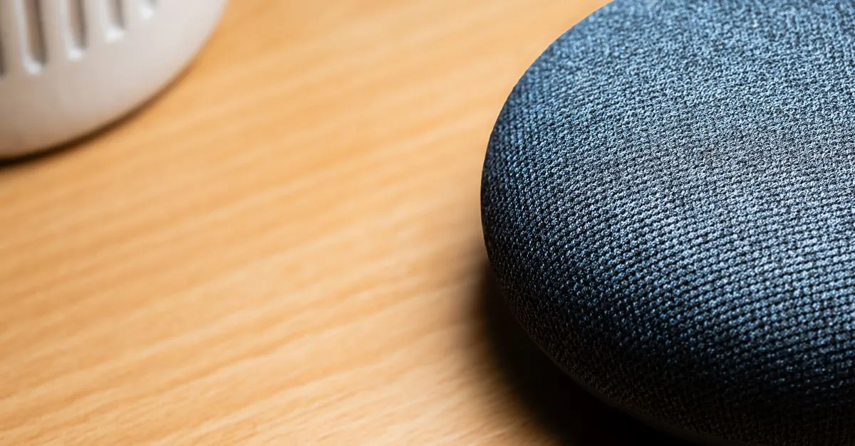 A close-up view of a smart speaker on a wooden table, capturing texture details.